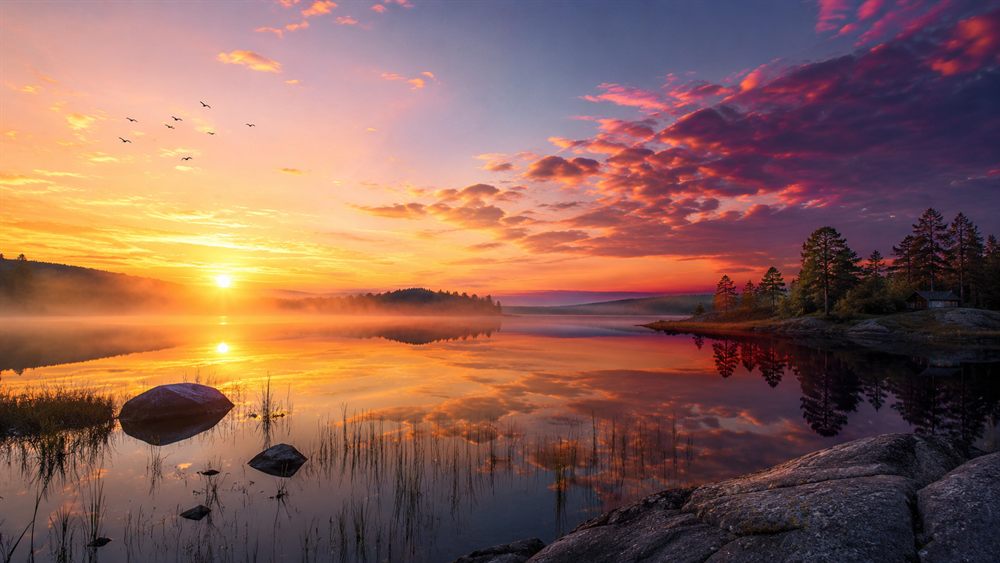Soluppgång över en spegelblank sjö i Norden med färgsprakande himmel